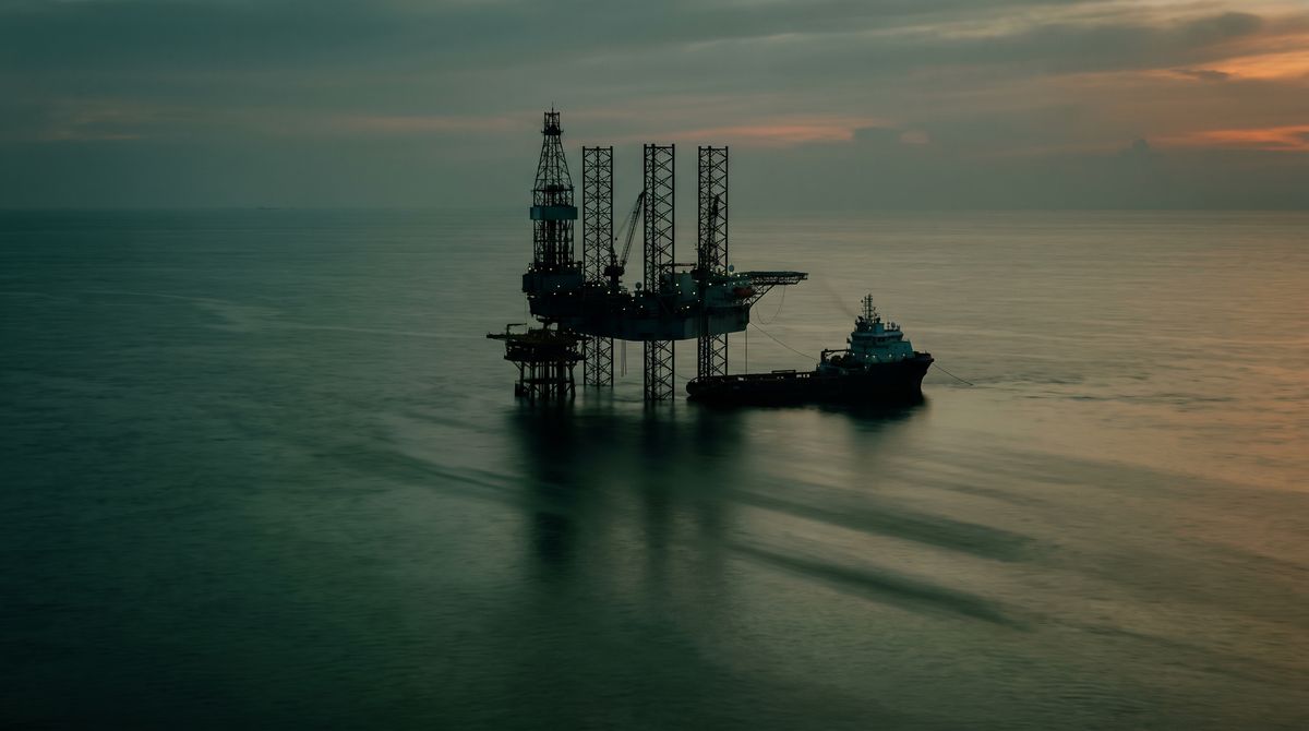 Jack-up drilling rig and a support vessel on a calm sea at sunset